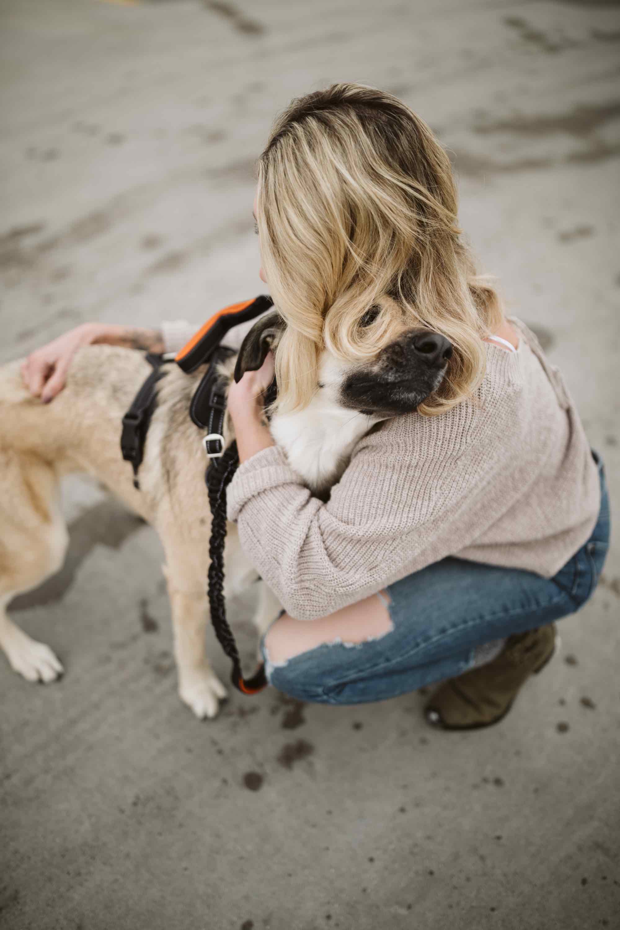 Blonde woman hugs tan dog on pavement outside.